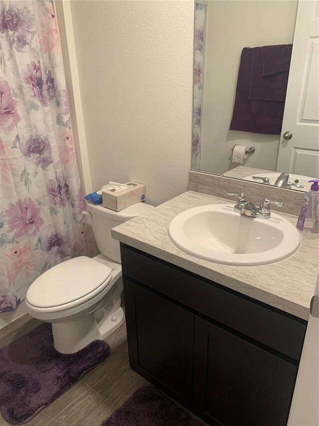 bathroom featuring hardwood / wood-style flooring, vanity, toilet, and curtained shower