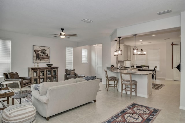 tiled living room with a textured ceiling, a healthy amount of sunlight, and ceiling fan with notable chandelier