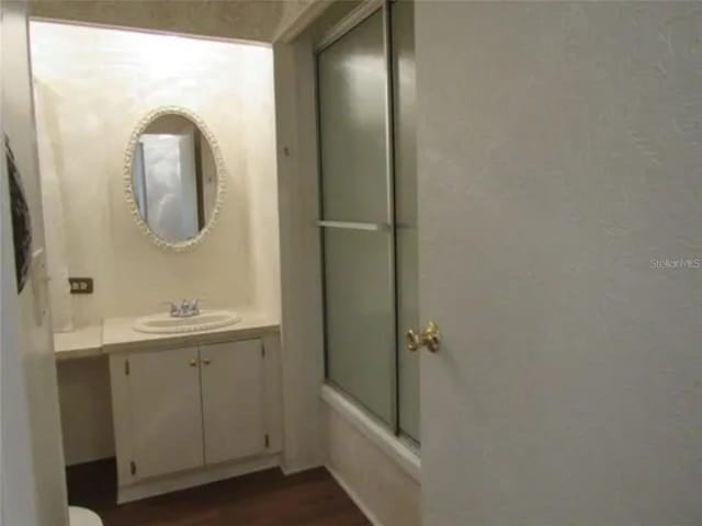 bathroom with combined bath / shower with glass door, wood-type flooring, and vanity