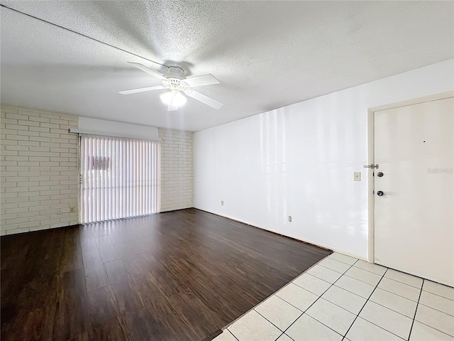 tiled empty room featuring ceiling fan, brick wall, and a textured ceiling