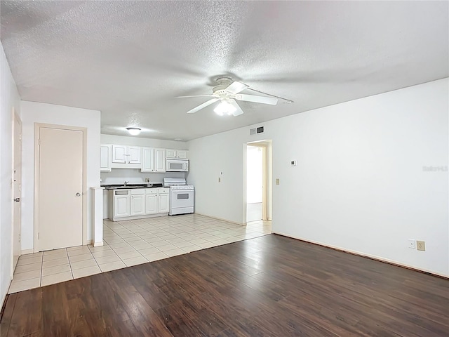 unfurnished living room with ceiling fan, sink, a textured ceiling, and light wood-type flooring