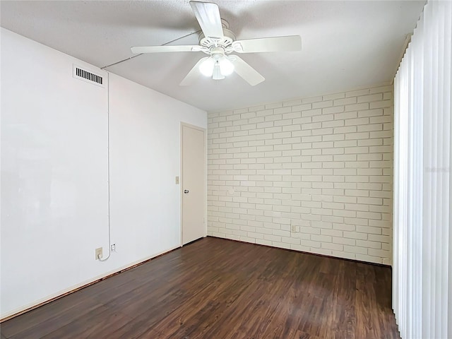 spare room featuring ceiling fan, dark hardwood / wood-style floors, and brick wall