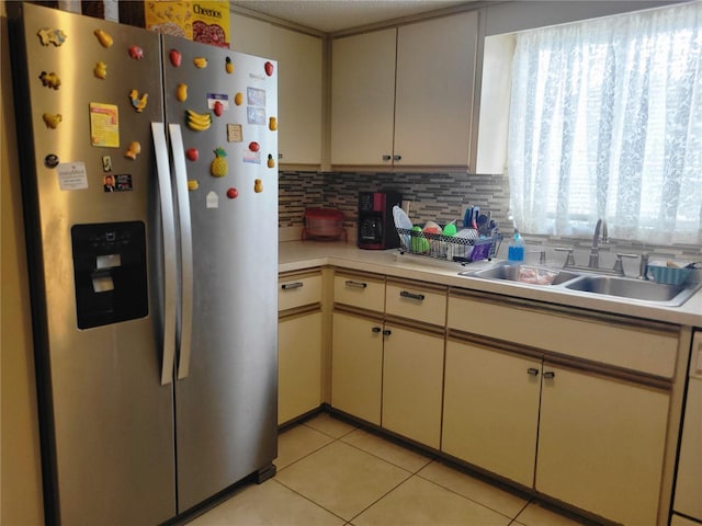 kitchen featuring light tile patterned floors, stainless steel fridge, backsplash, cream cabinets, and sink