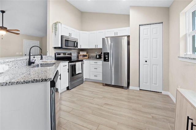 kitchen with appliances with stainless steel finishes, a sink, light stone counters, light wood finished floors, and white cabinets