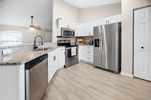 kitchen with stainless steel appliances, a sink, a peninsula, light stone countertops, and white cabinets