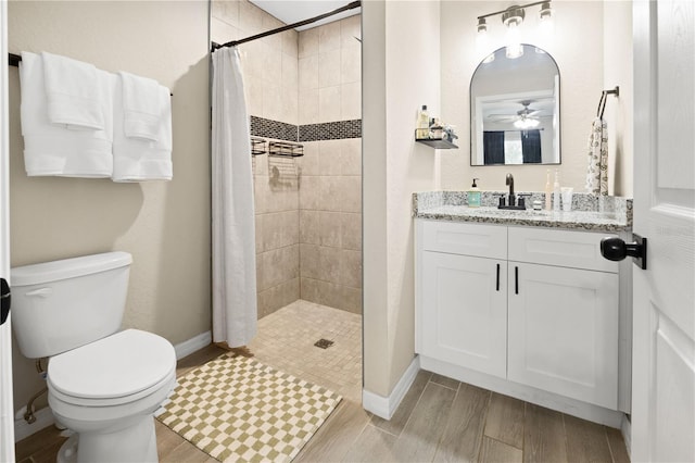 bathroom with a tile shower, toilet, ceiling fan, and vanity