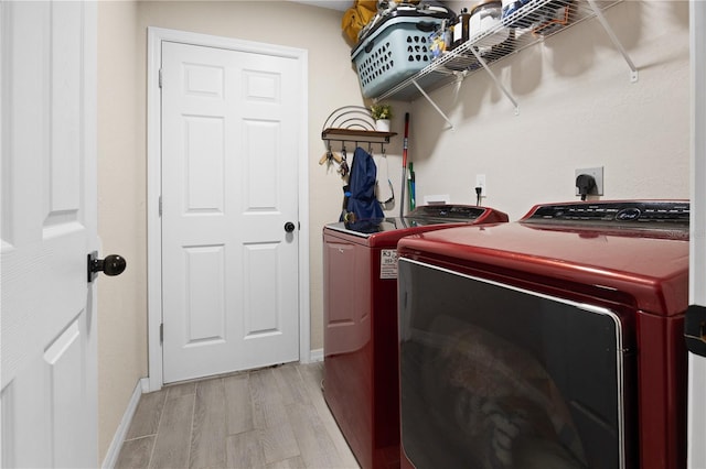 clothes washing area with washing machine and dryer, light wood-type flooring, and baseboards
