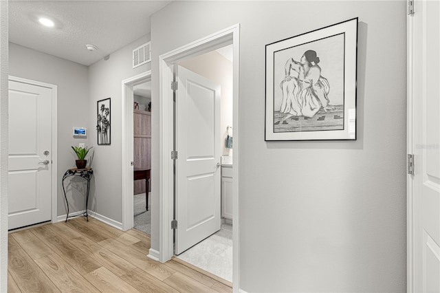 hallway with a textured ceiling and light hardwood / wood-style floors