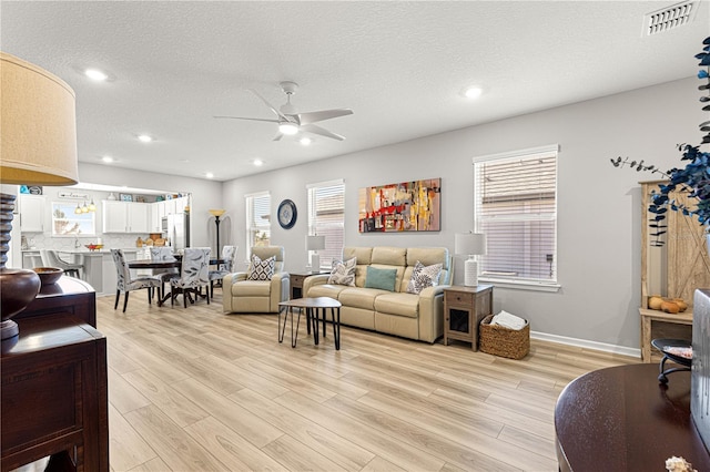 living room featuring a textured ceiling, ceiling fan, and light wood-type flooring