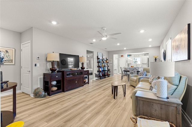 living room featuring light wood-type flooring, ceiling fan, and a textured ceiling