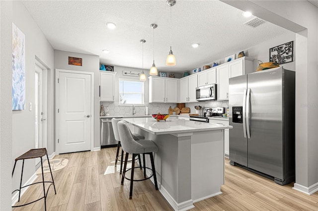 kitchen with backsplash, a kitchen island, hanging light fixtures, stainless steel appliances, and white cabinets