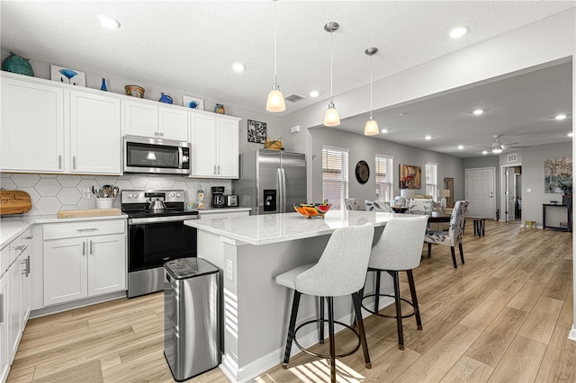 kitchen with white cabinets, appliances with stainless steel finishes, a center island, decorative backsplash, and ceiling fan