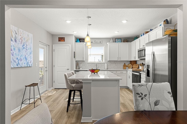 kitchen with appliances with stainless steel finishes, decorative backsplash, pendant lighting, white cabinets, and a center island