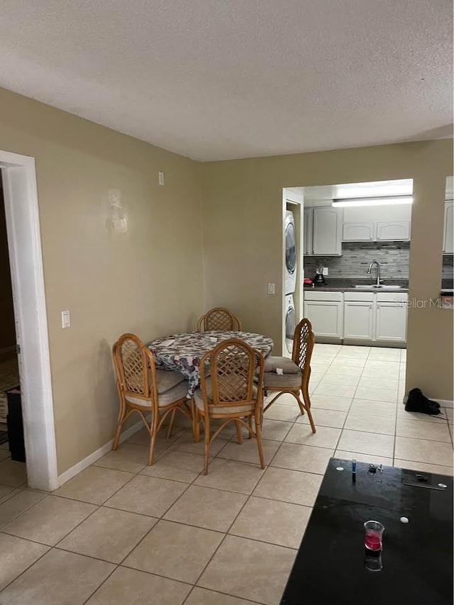 dining area with a textured ceiling, light tile patterned flooring, stacked washer / dryer, and sink