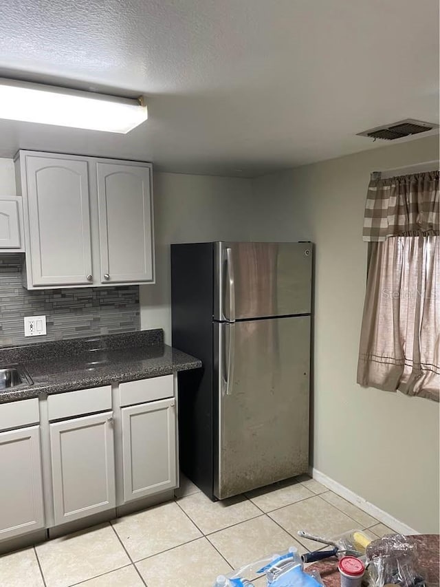 kitchen with decorative backsplash, sink, stainless steel refrigerator, white cabinetry, and light tile patterned flooring