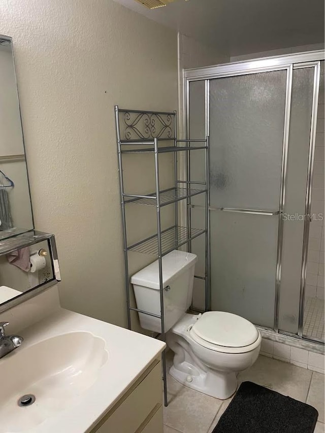 bathroom featuring toilet, vanity, a shower with door, and tile patterned floors