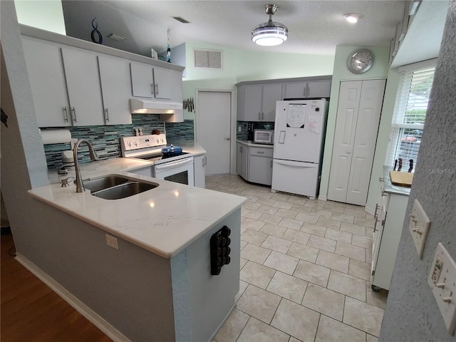 kitchen with tasteful backsplash, vaulted ceiling, kitchen peninsula, sink, and white appliances