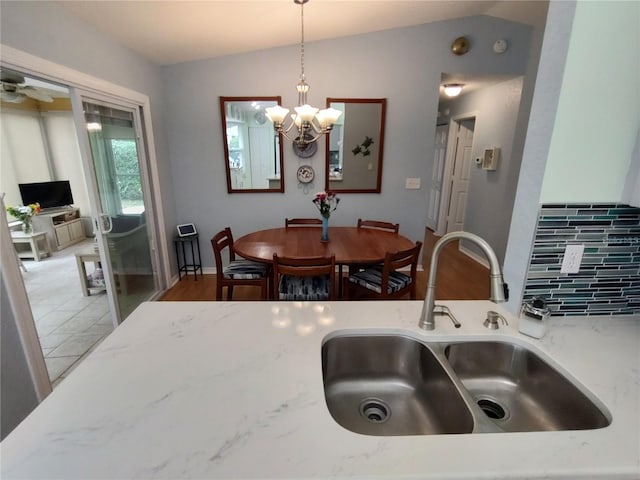 kitchen featuring hanging light fixtures, vaulted ceiling, sink, and light stone counters