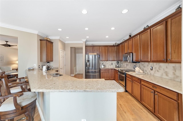 kitchen featuring kitchen peninsula, a breakfast bar area, appliances with stainless steel finishes, light stone countertops, and sink