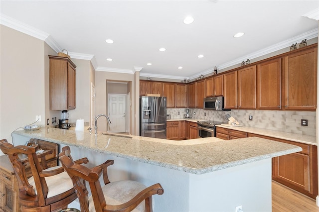 kitchen with appliances with stainless steel finishes, sink, kitchen peninsula, light stone counters, and a breakfast bar area