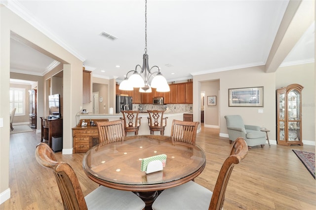 dining space with crown molding, light hardwood / wood-style floors, and a notable chandelier