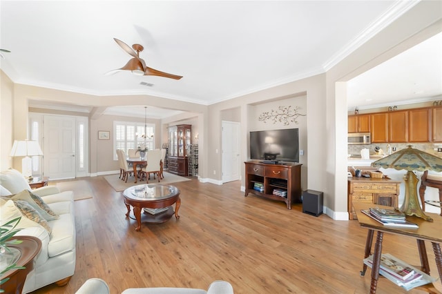 living room with ceiling fan with notable chandelier, light hardwood / wood-style flooring, and ornamental molding