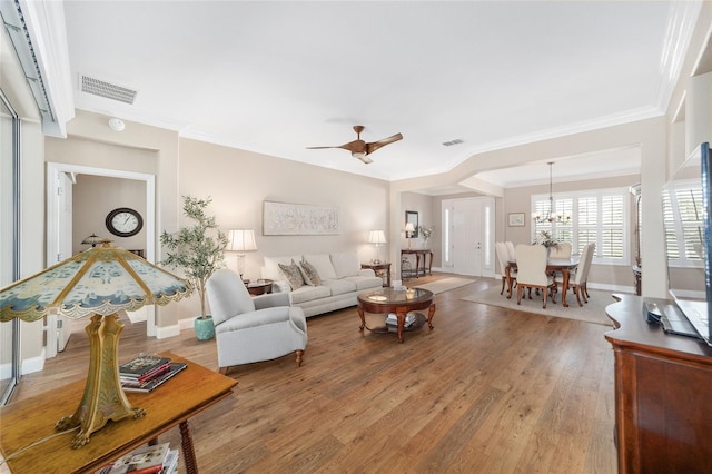 living room featuring ornamental molding, ceiling fan with notable chandelier, and wood-type flooring