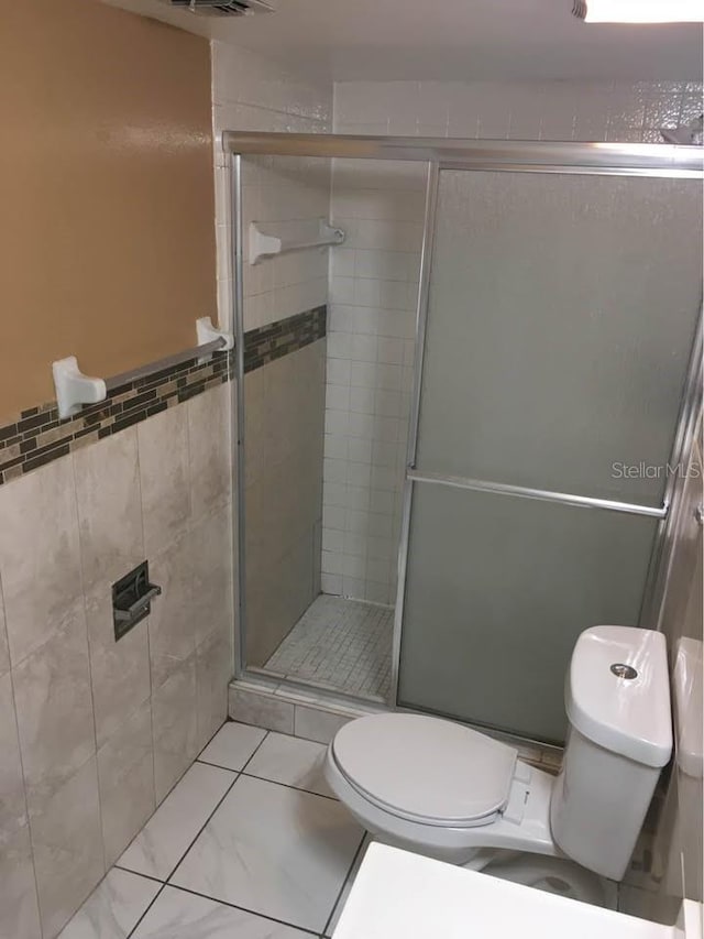 bathroom featuring toilet, tile patterned flooring, tile walls, and walk in shower