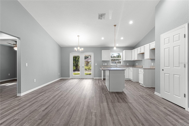 kitchen with lofted ceiling, hardwood / wood-style floors, a kitchen island, white cabinetry, and hanging light fixtures