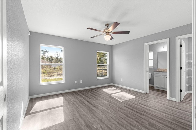 unfurnished bedroom with ceiling fan, connected bathroom, wood-type flooring, and multiple windows