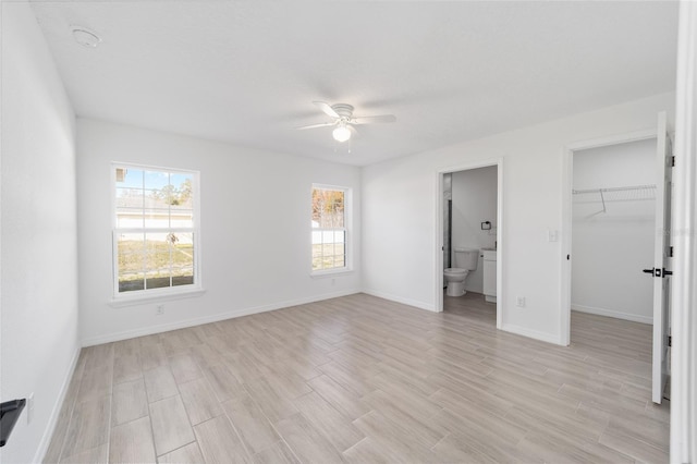 unfurnished bedroom with multiple windows, a spacious closet, ceiling fan, and ensuite bathroom