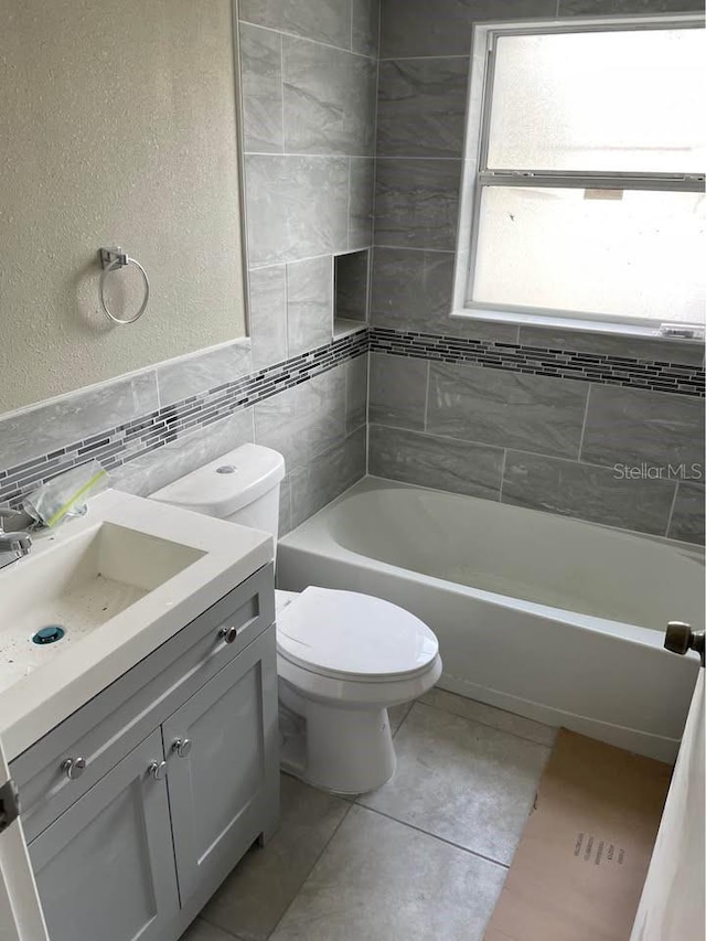 full bathroom with tiled shower / bath combo, tile patterned floors, vanity, tile walls, and toilet