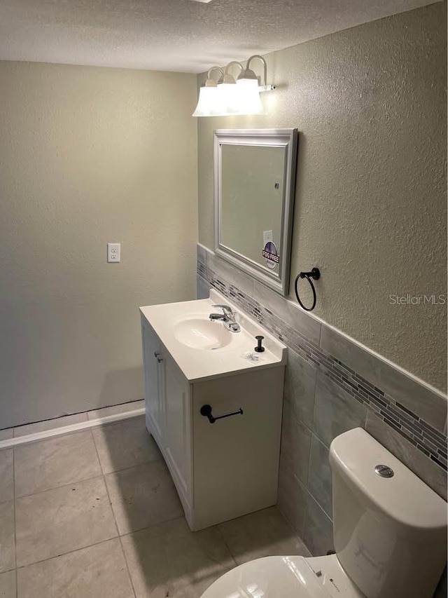 bathroom with toilet, a textured ceiling, vanity, and tile walls