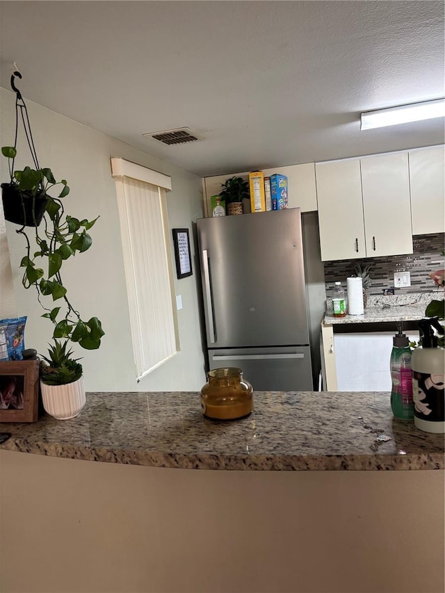 kitchen featuring white cabinets, tasteful backsplash, and stainless steel refrigerator