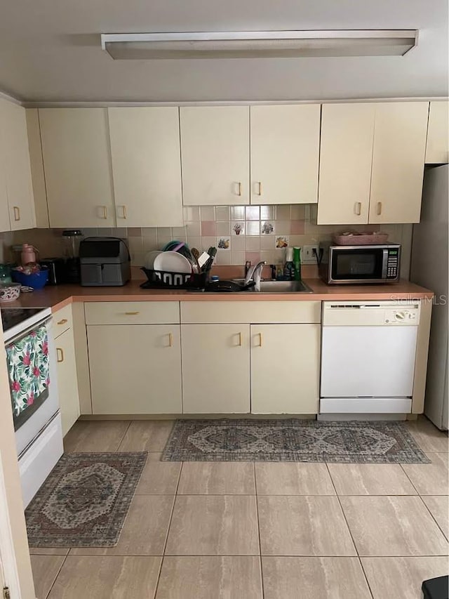 kitchen featuring tasteful backsplash, sink, appliances with stainless steel finishes, light tile patterned floors, and cream cabinetry