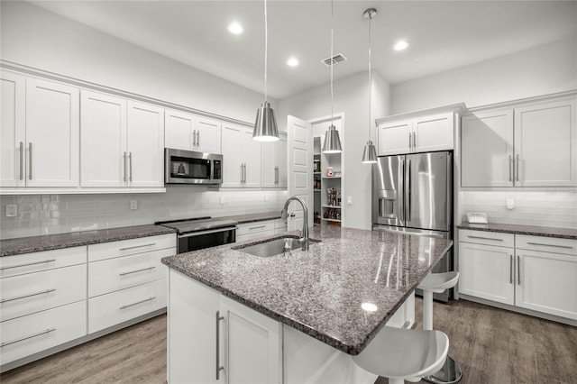 kitchen with backsplash, a center island with sink, sink, hanging light fixtures, and appliances with stainless steel finishes