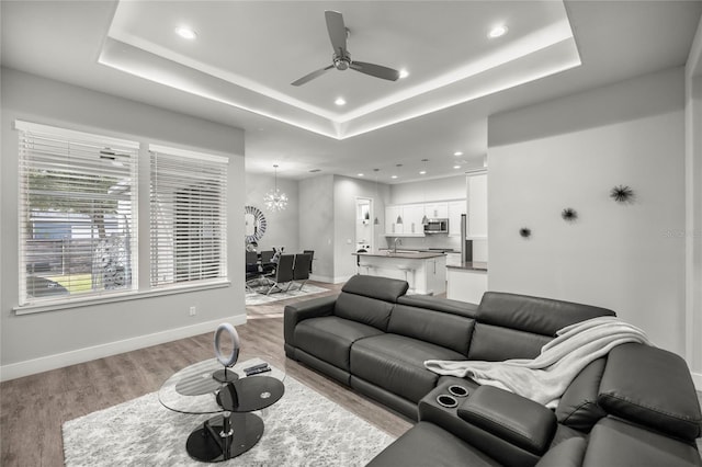 living room featuring light hardwood / wood-style floors, a tray ceiling, and ceiling fan with notable chandelier