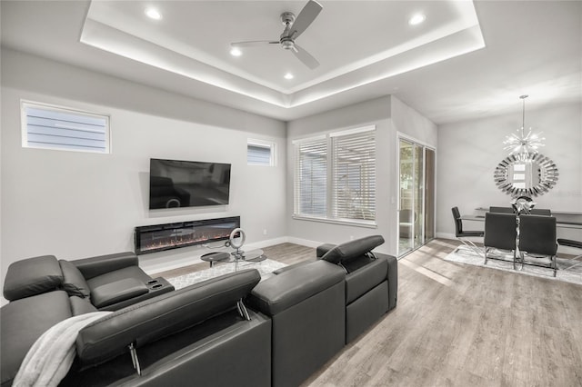 living room featuring ceiling fan with notable chandelier, a tray ceiling, and light hardwood / wood-style flooring