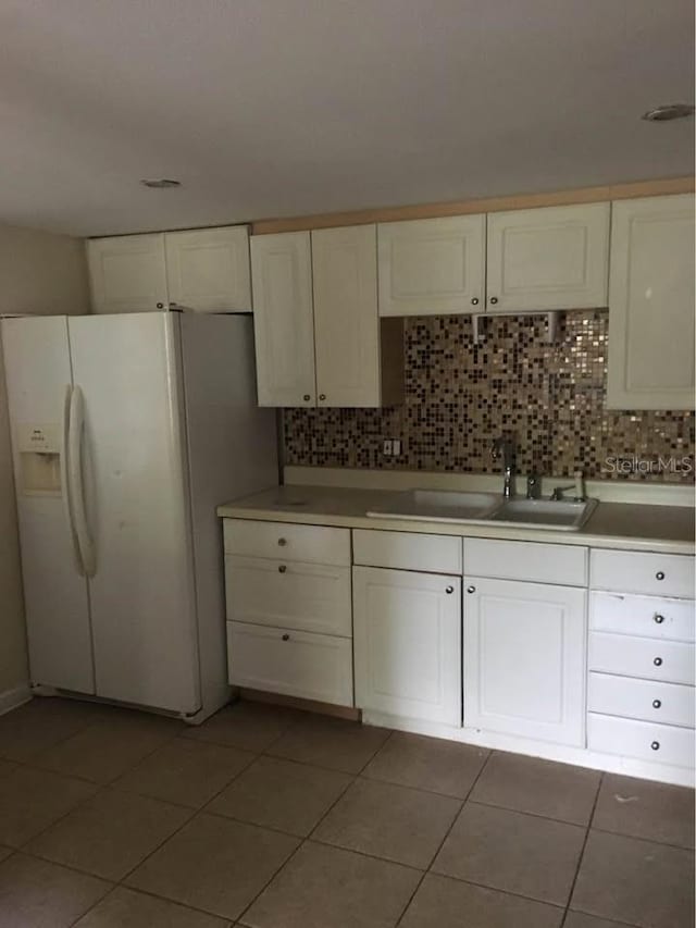 kitchen featuring white fridge with ice dispenser, tile patterned flooring, white cabinetry, decorative backsplash, and sink