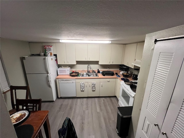 kitchen with sink, white cabinets, white appliances, light hardwood / wood-style floors, and a textured ceiling