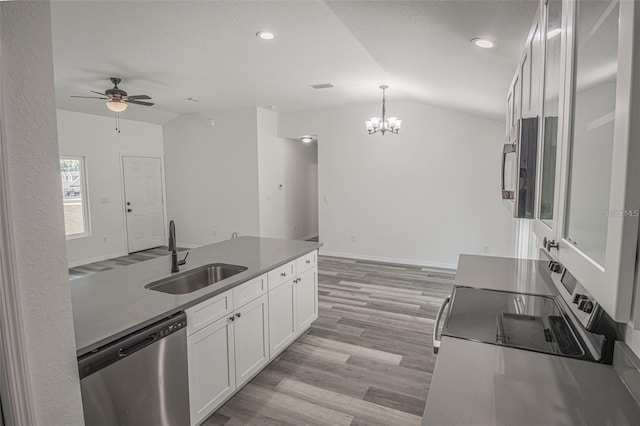 kitchen with appliances with stainless steel finishes, lofted ceiling, hanging light fixtures, white cabinets, and sink