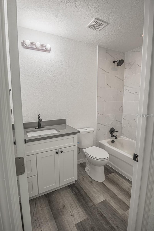 full bathroom featuring toilet, vanity, tiled shower / bath, hardwood / wood-style flooring, and a textured ceiling