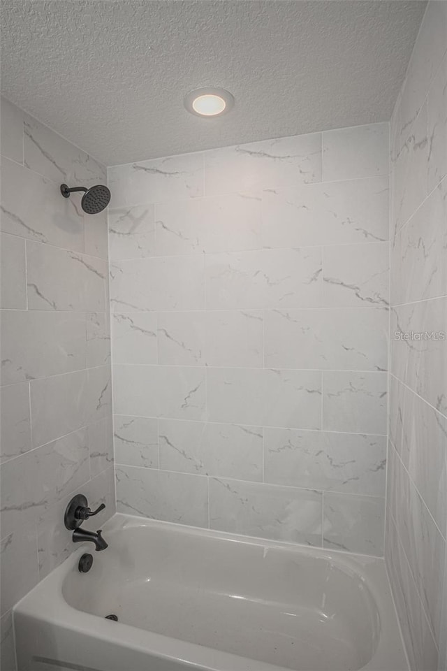 bathroom with a textured ceiling and tiled shower / bath combo