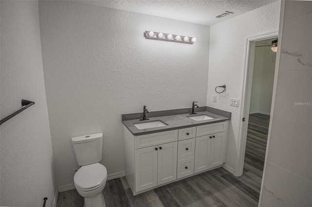 bathroom featuring toilet, vanity, ceiling fan, wood-type flooring, and a textured ceiling