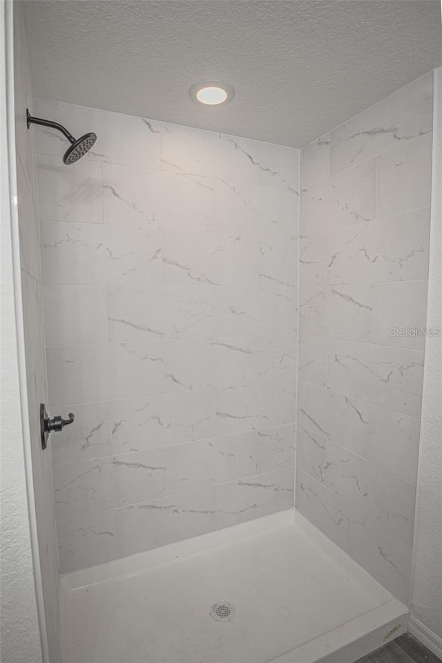 bathroom with a textured ceiling and tiled shower