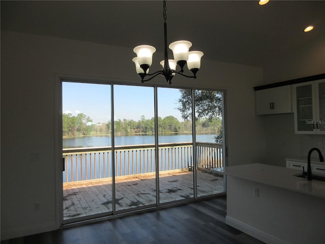 unfurnished dining area featuring dark wood-type flooring, a water view, a sink, and baseboards