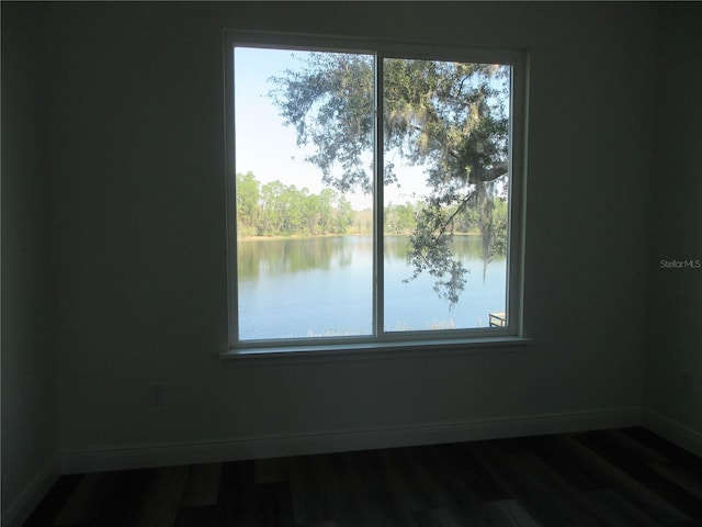 empty room featuring a water view, baseboards, and wood finished floors