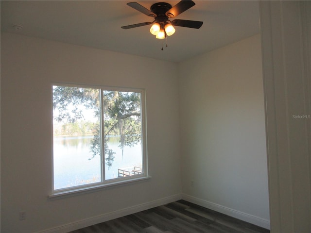 unfurnished room featuring dark wood-type flooring, a water view, plenty of natural light, and baseboards