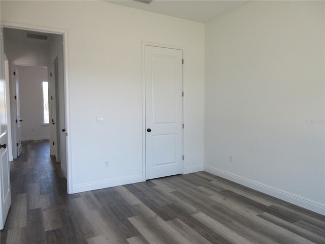 unfurnished bedroom with dark wood-style floors, visible vents, and baseboards