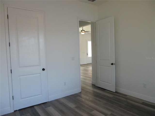 spare room with dark wood-style flooring, visible vents, and baseboards